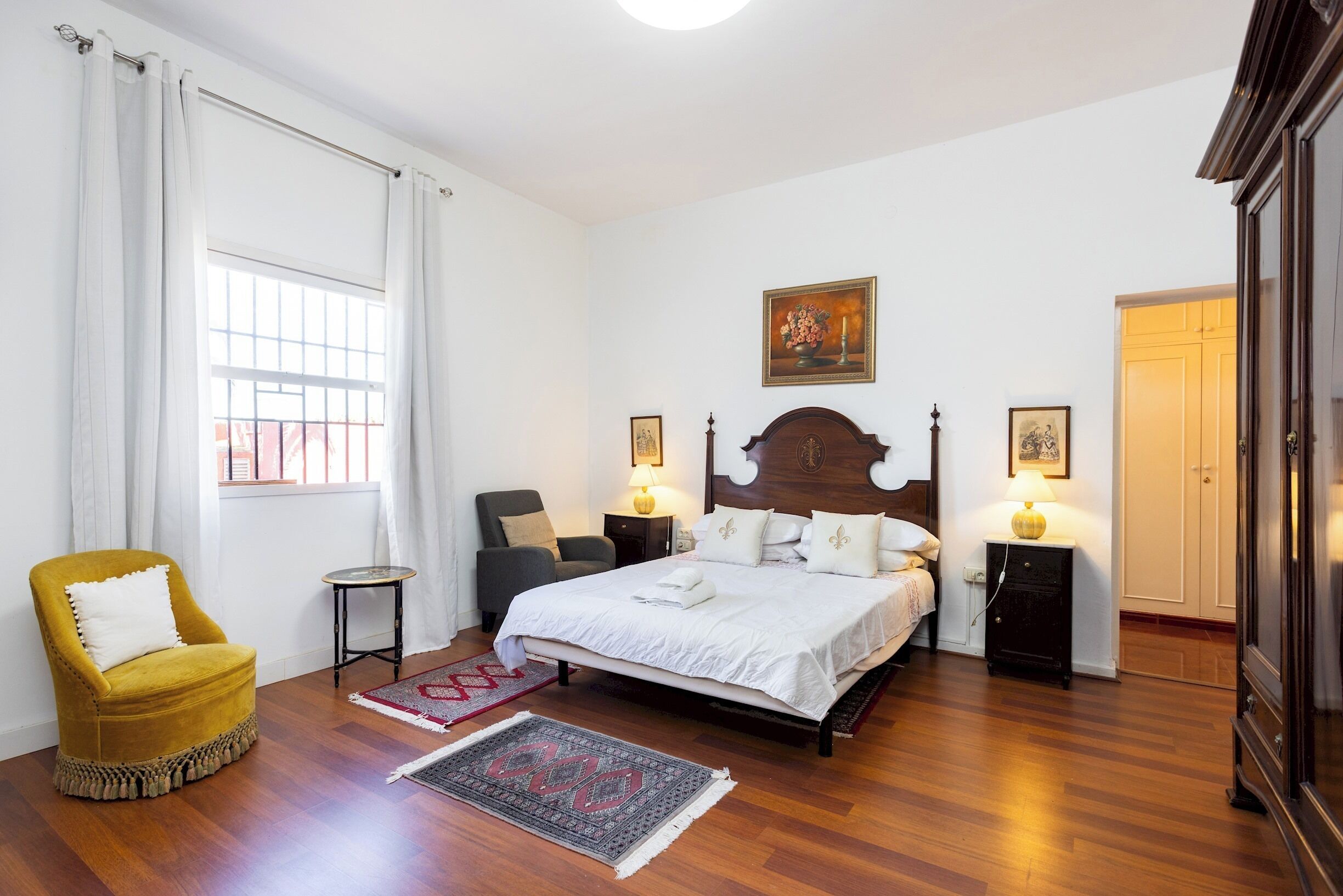 A bedroom with a large bed, two bedside tables, a chair, a small table, and a wardrobe.