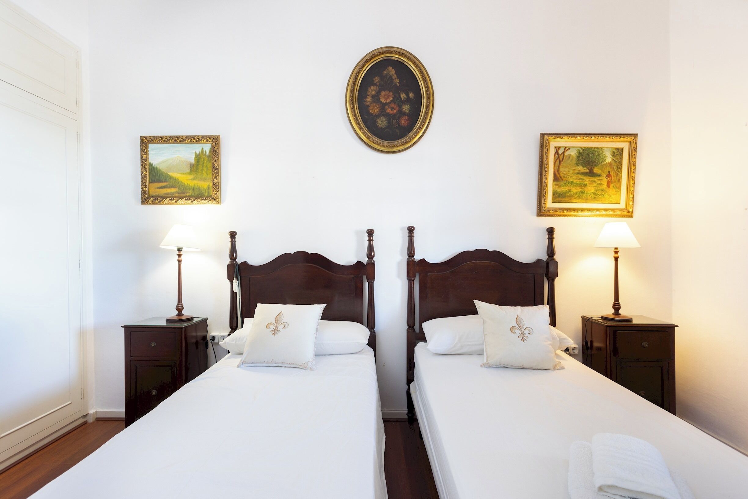 A double room with two beds, each with a nightstand and a lamp. There are two framed pictures on the wall above the beds.