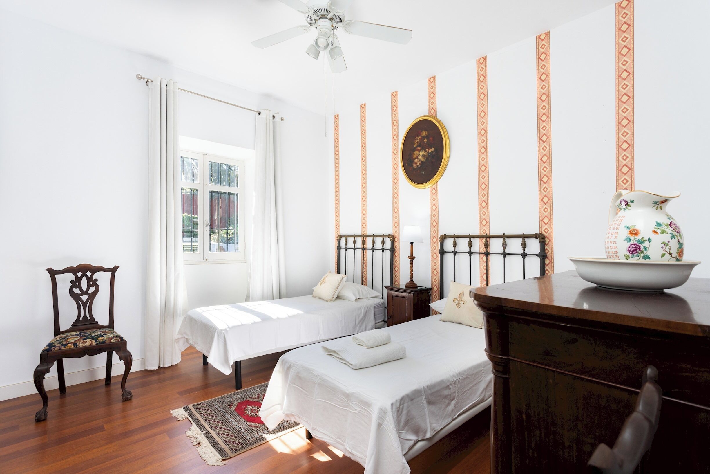 Habitación de hotel con dos camas, una silla de madera, un escritorio con un florero y decoraciones de pared estampadas.