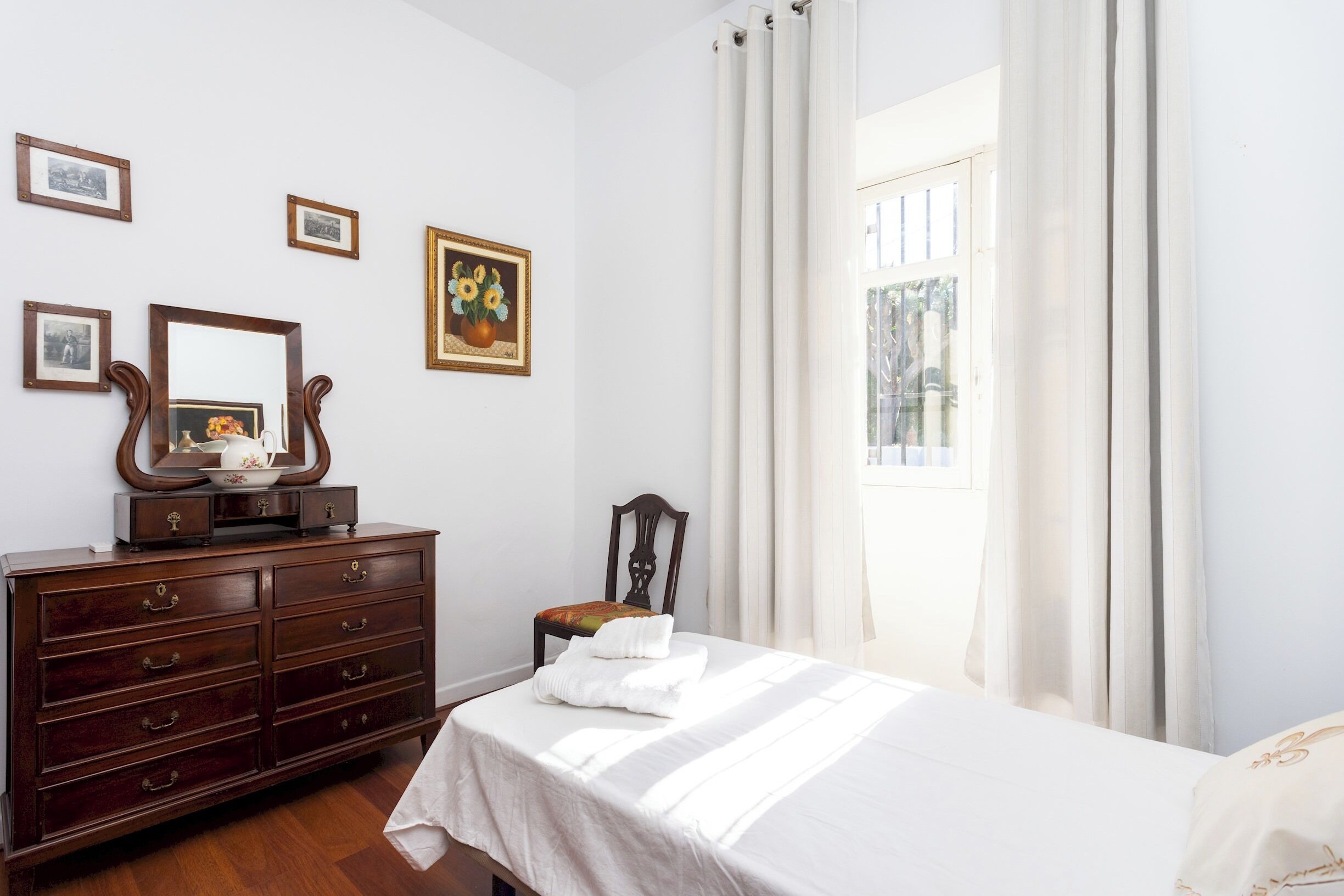 Un dormitorio con un aparador de madera, una cama con ropa de cama blanca y una ventana con cortinas.