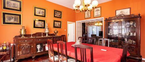 Ein Esszimmer mit rotem Tischblatt, Holzsesseln, einer Kristallleuchter und gerahmten Bildern an der Wand.