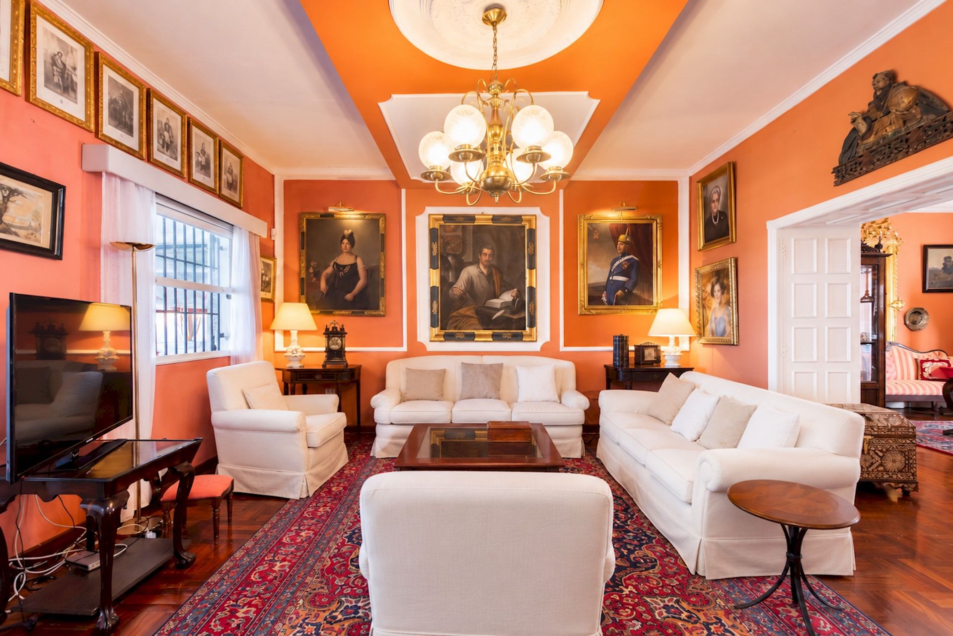 Un salon avec un téléviseur, des canapés blancs, un tapis à motifs et des portraits encadrés accrochés aux murs.