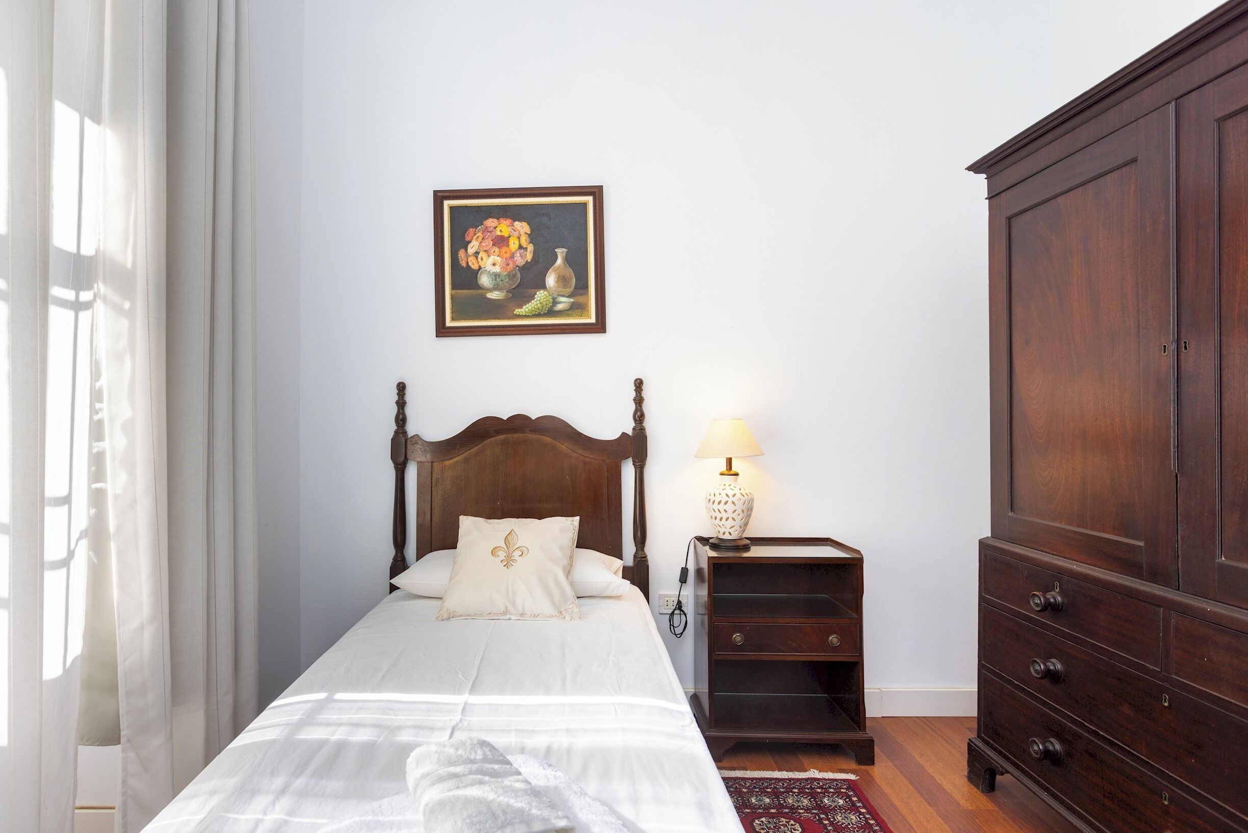 Ein Schlafzimmer mit einem hölzernen Bett, einem Nachttisch mit Lampe, einer Kommode und einem Bild an der Wand.