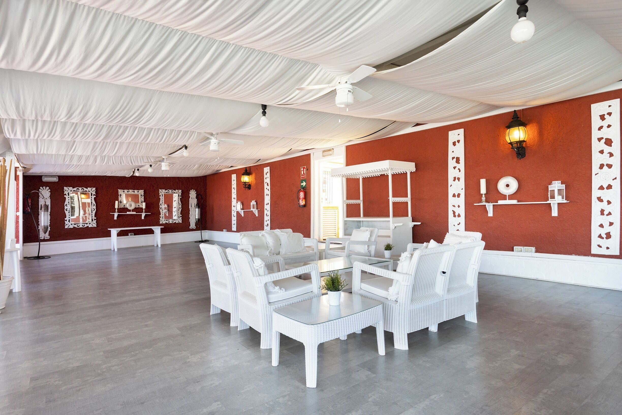 A spacious room with white wicker furniture, a glass coffee table, and a red accent wall.