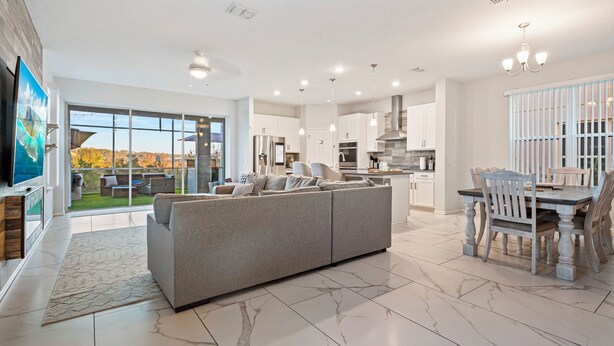 A modern kitchen with white cabinetry, a dining area with a wooden table and chairs, and a grey sofa in the living area. - Costa Championsgate 4BDR - Quiet House with Jacuzzi (Davenport)