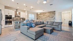 A modern kitchen with built-in appliances, a dining area with a wooden accent wall, and a grey sectional sofa in a spacious living room. - Costa Championsgate 4BDR - Quiet House with Jacuzzi (Davenport)