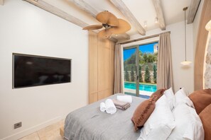 Une chambre avec un lit, une télévision, un ventilateur de plafond et une vue sur une piscine.