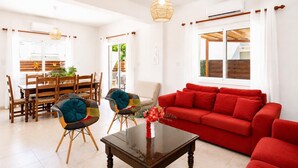A living room with a red sofa, a glass coffee table, and a dining area with wooden chairs and a table. - Argiro Bright Villa - Four Bedroom Villa, Sleeps 8 (Pernera)