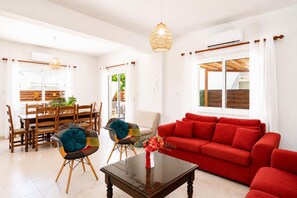 Una sala de estar con un sofá rojo, una mesa de centro de vidrio y un comedor con sillas y mesa de madera.