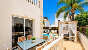A patio with a glass table, chairs, and a small pool area with lounge chairs. - Argiro Bright Villa - Four Bedroom Villa, Sleeps 8 (Pernera)