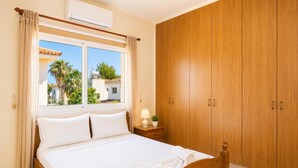 A hotel room with a bed, a window, a wardrobe, and a nightstand with a lamp and a plant. - Argiro Bright Villa - Four Bedroom Villa, Sleeps 8 (Pernera)