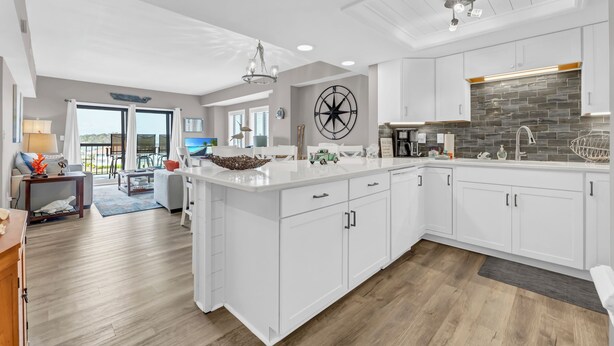 A spacious kitchen with white cabinetry, a large island, and a stone backsplash. - Renovated 3-Bedroom Condo, Large Pool, Beach Access & Views! (North Myrtle Beach)