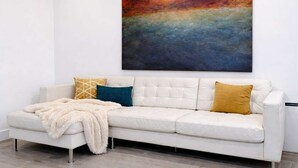 Ein weißes Sofa mit einer flauschigen Decke, zwei gemusterten Kissen und einem großen, abstrakten Gemälde an der Wand.