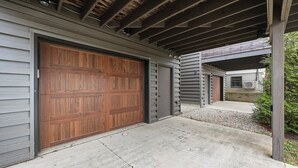 Eine Garage mit Holztür, Betonauffahrt und überdachter Terrasse.