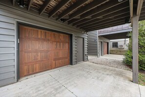 A garage with a wooden door, a concrete driveway, and a covered patio area. - Modern studio apartment with dedicated workspace! (Louisville)