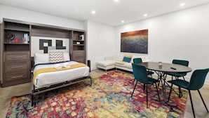 Ein modernes Schlafzimmer mit Bett, Sofa, Esstisch und Stühlen sowie einem farbenfrohen Teppich.