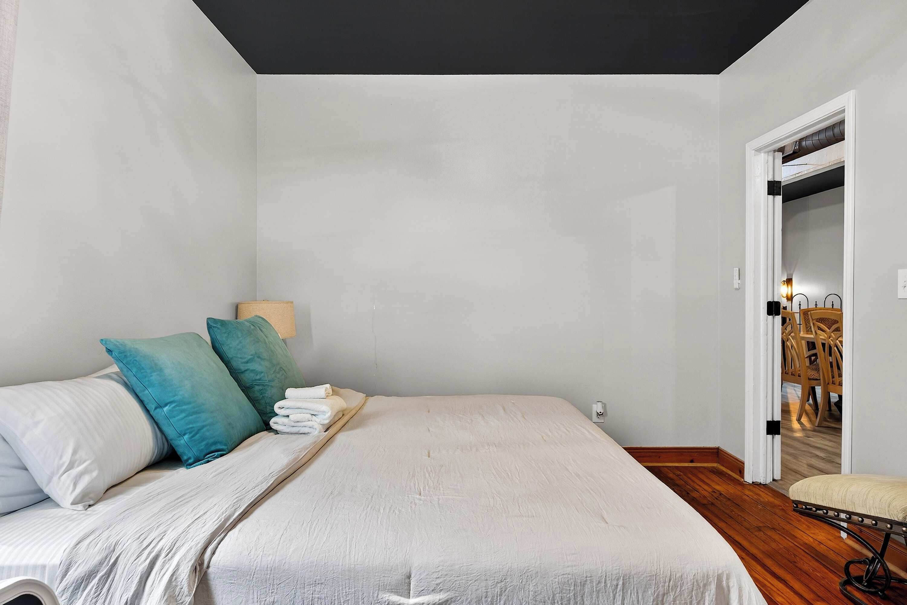 Un dormitorio con cama, almohadas, una mesita de noche, lámpara y una puerta que da al baño.