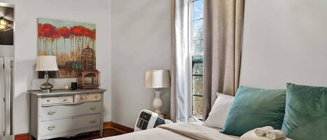 Ein Schlafzimmer mit Bett, Nachttisch mit Lampe, einem Bild an der Wand und einem Fenster mit Vorhängen.