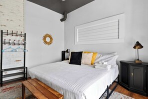 Een slaapkamer met een bed, een houten bankje, een radiator, een wandplank, een decoratieve zonnespiegel en een zwarte kast.