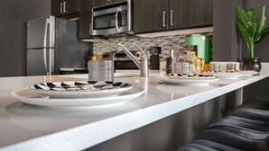 Una cocina moderna con electrodomésticos de acero inoxidable, encimera blanca y armarios de madera oscura.