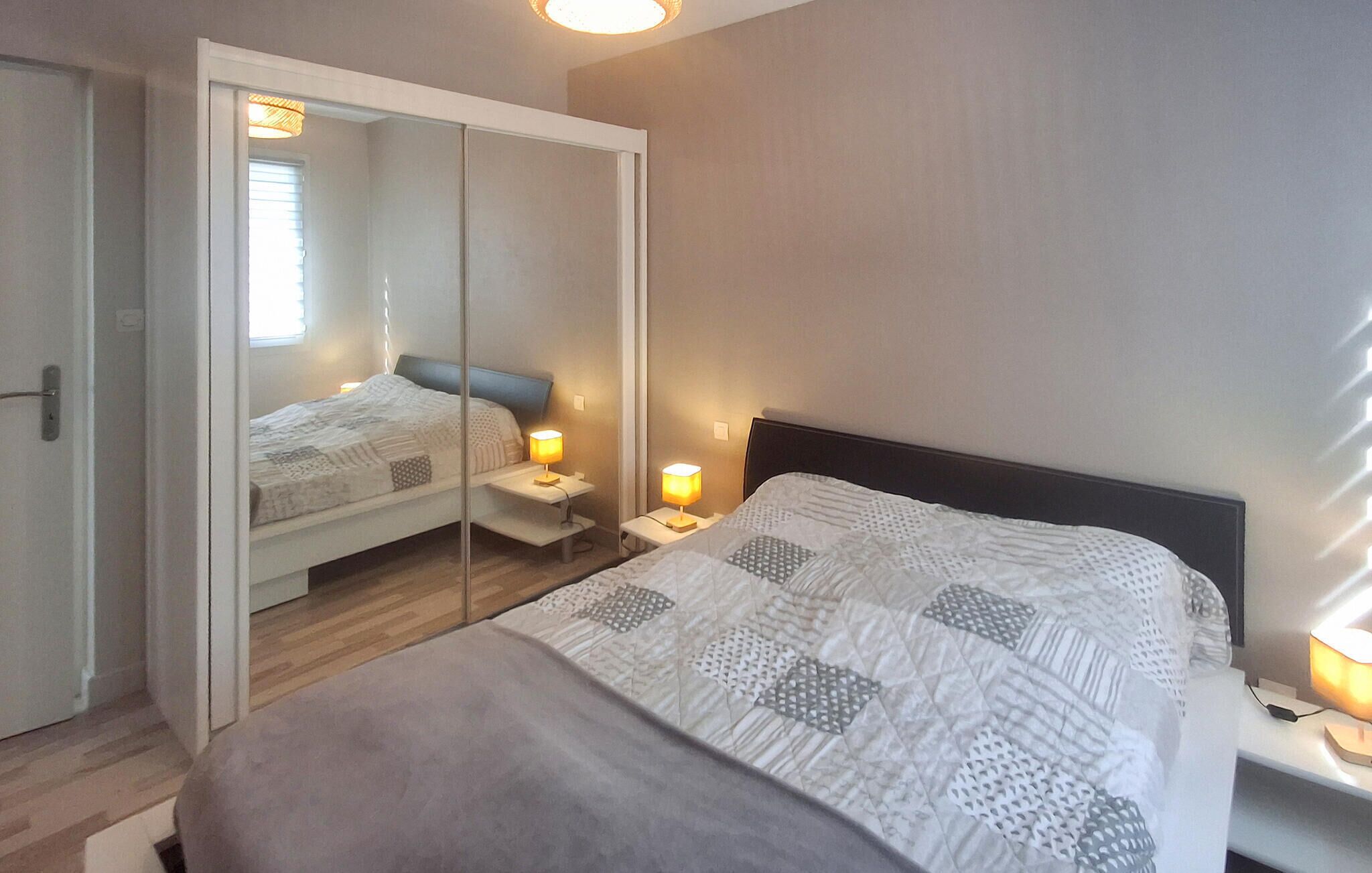 Een slaapkamer met een bed, nachtlampjes, een spiegel en een kledingkast.