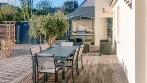 Une terrasse extérieure avec une table et des chaises, un barbecue et un espace salon abrité.