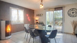 Un coin repas avec une table en verre, quatre chaises, une cheminée, une horloge et une vue sur la verdure grâce à une porte coulissante.