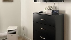 Una habitación con un aparador negro, un radiador blanco, un aire acondicionado blanco y una televisión de pantalla plana montada en la pared.