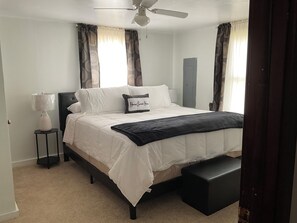 Een slaapkamer met een bed, nachtkastje, lamp en een plafondventilator.