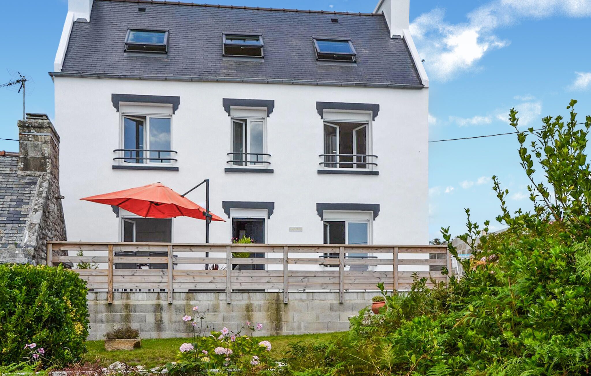 A white two-story building with multiple windows, a red umbrella, and a wooden fence.