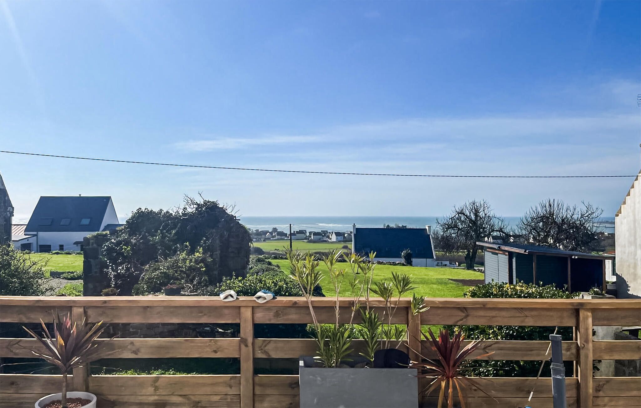 En træterrasse med plantekasser, med udsigt over et boligområde med huse og en klar himmel.