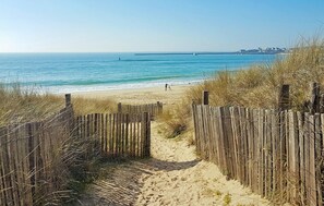 A sandy beach path leading to the ocean, with a wooden fence on one side and a clear view of the sea and distant buildings. - Nice home in Plouhinec with house sea view (Plouhinec)