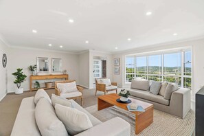 Ein geräumiges Wohnzimmer mit großem Fenster und Blick ins Freie, ausgestattet mit einer Couch, einem Couchtisch und einem Essbereich mit Holztisch und Stühlen.