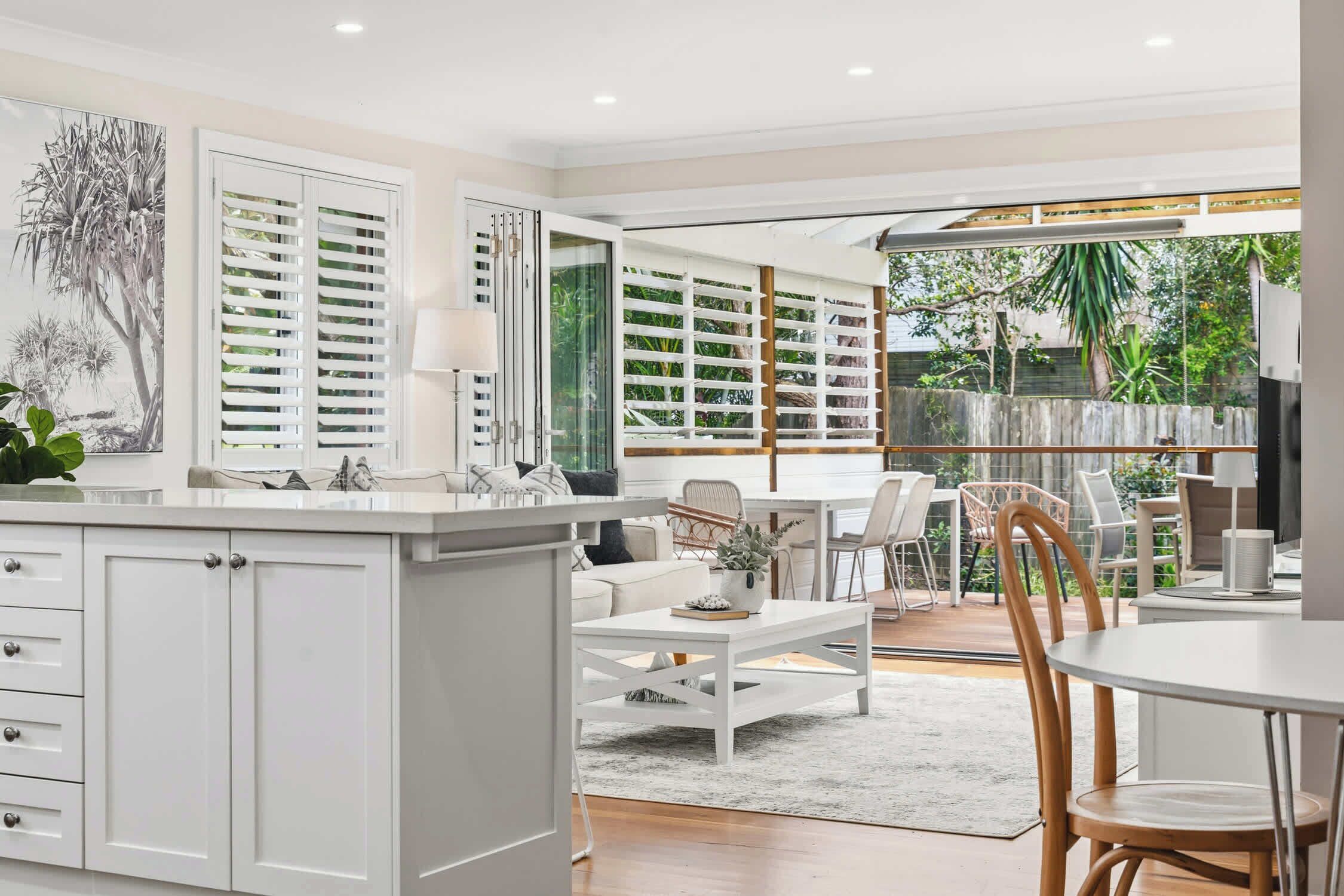 A modern kitchen with white cabinetry, a dining area with white furniture, and a view of the outdoors.