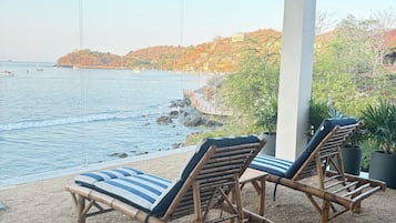 Un espace extérieur abrité, aménagé avec deux fauteuils de relaxation en bambou et offrant une vue sur la mer.