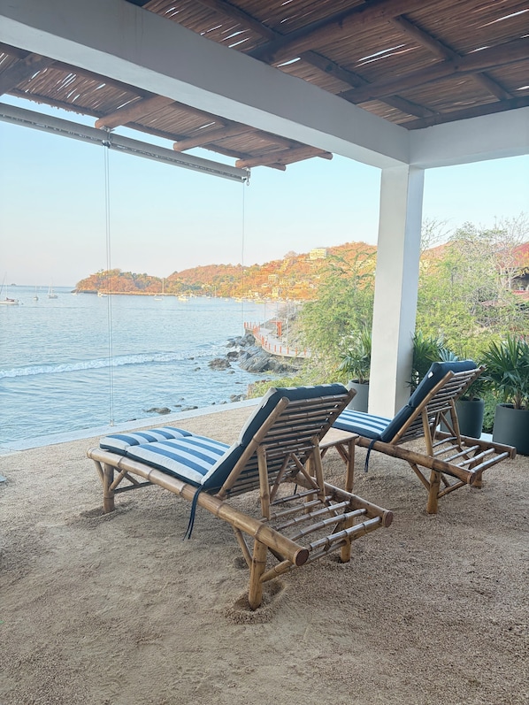 Un espace extérieur abrité, aménagé avec deux fauteuils de relaxation en bambou et offrant une vue sur la mer.