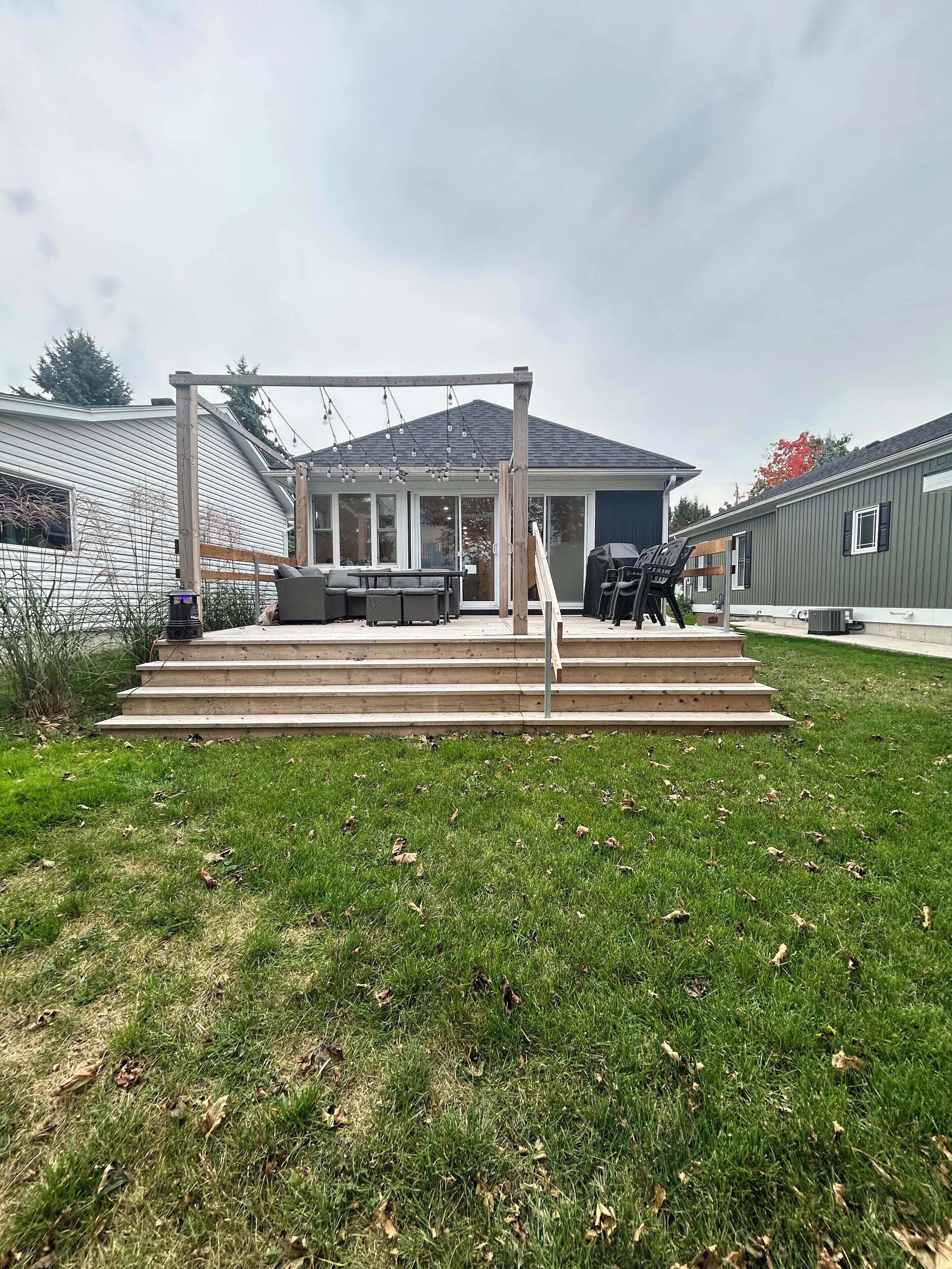 A backyard with a wooden pergola, outdoor seating, and a barbecue grill.