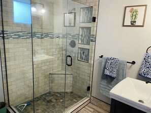 Une salle de bain moderne avec une douche à parois de verre, des murs carrelés, un lavabo et des serviettes décoratives.