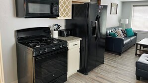 A compact kitchen with a stove, microwave, and refrigerator, adjacent to a living area with a sofa and a coffee table. - Newley Remodeled  3-bedroom house with AC in Grand Junction. (Grand Junction)