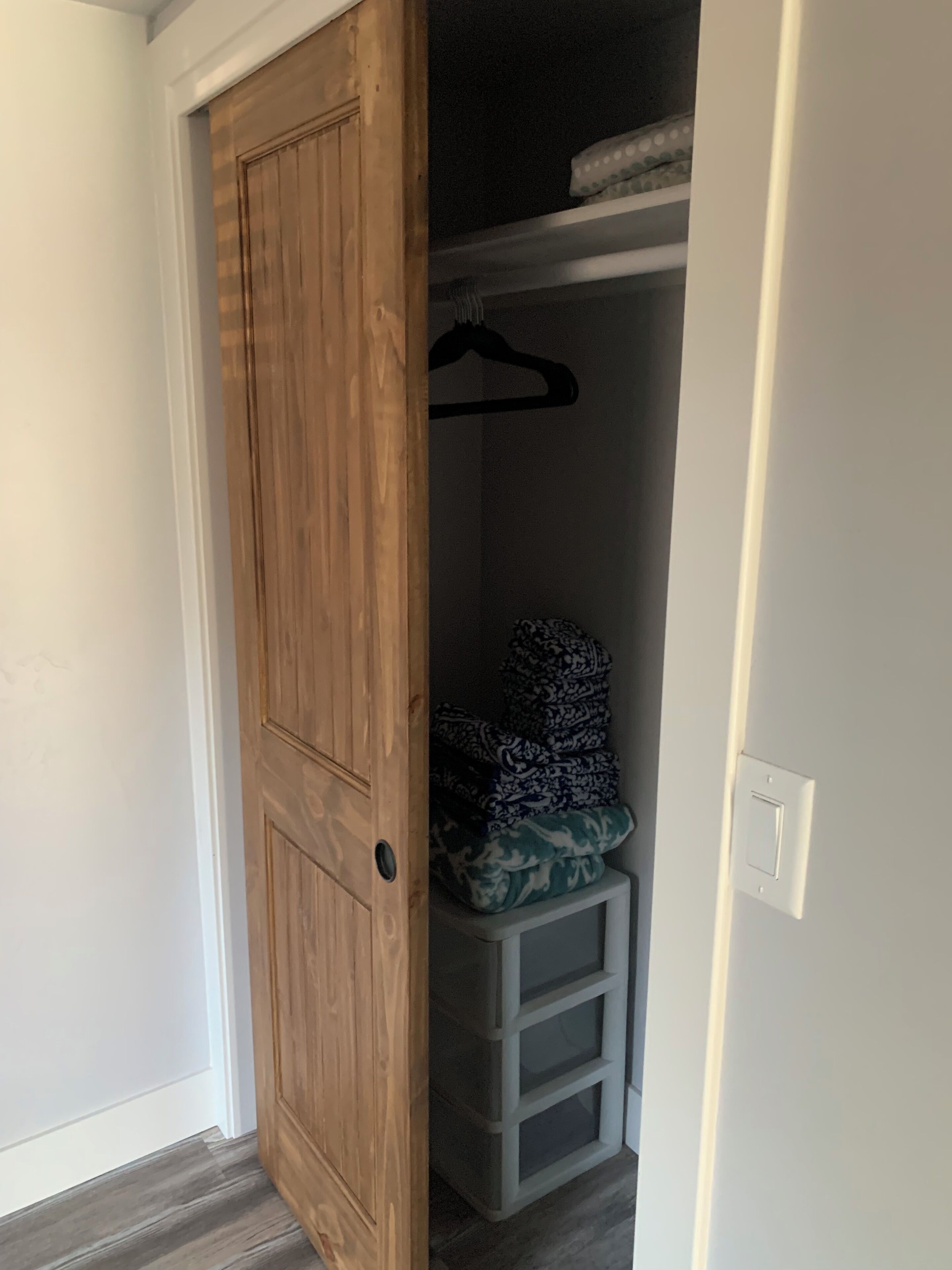 Puerta de madera que da a un armario con un perchero y mantas dobladas.