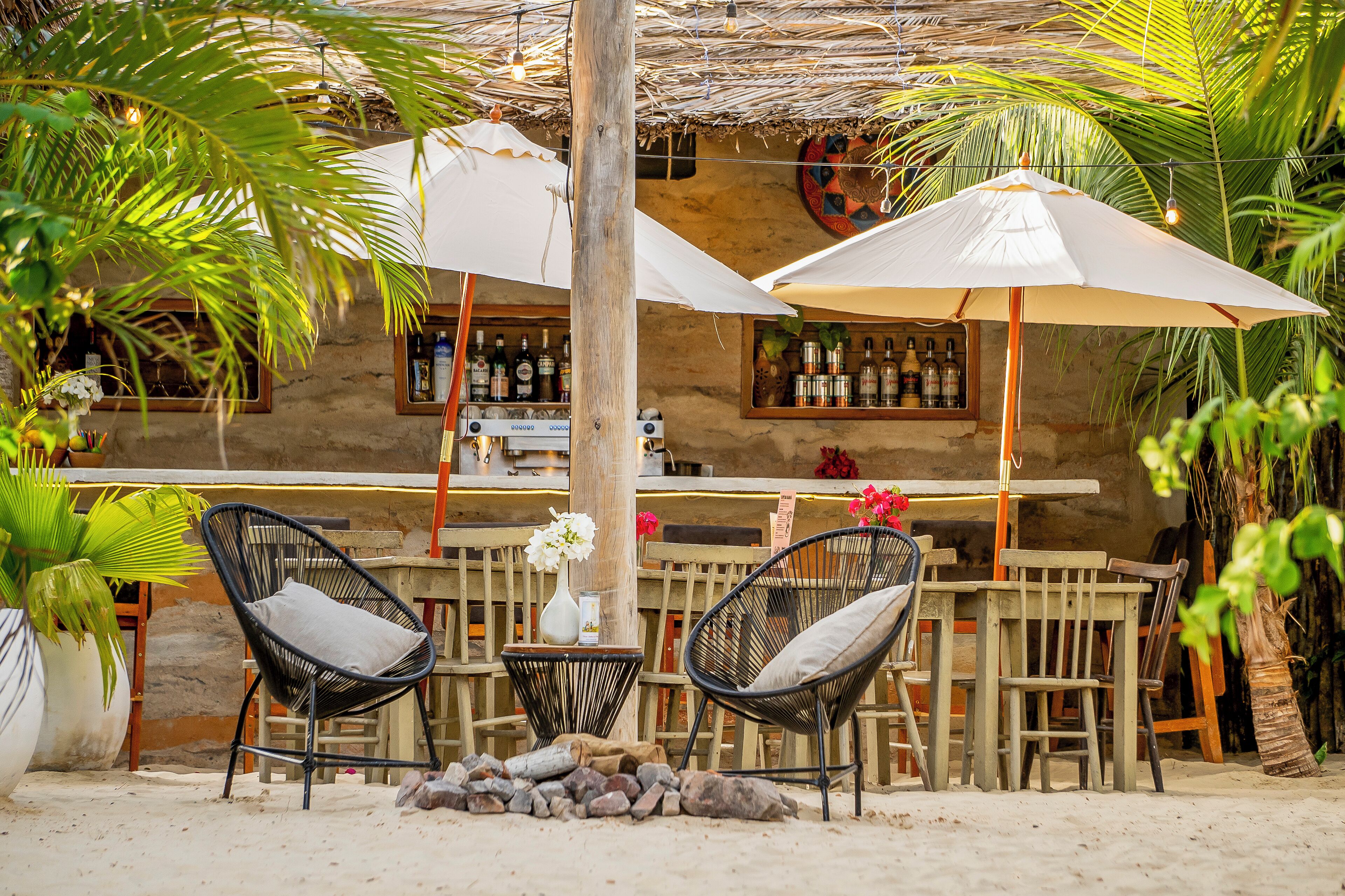 Un área de bar al aire libre con encanto rústico, mobiliario de madera, techo de paja y plantas tropicales.