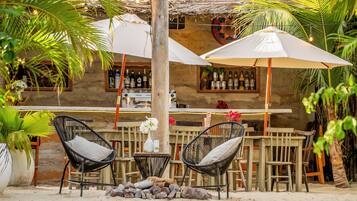 Un área de bar al aire libre con encanto rústico, mobiliario de madera, techo de paja y plantas tropicales.