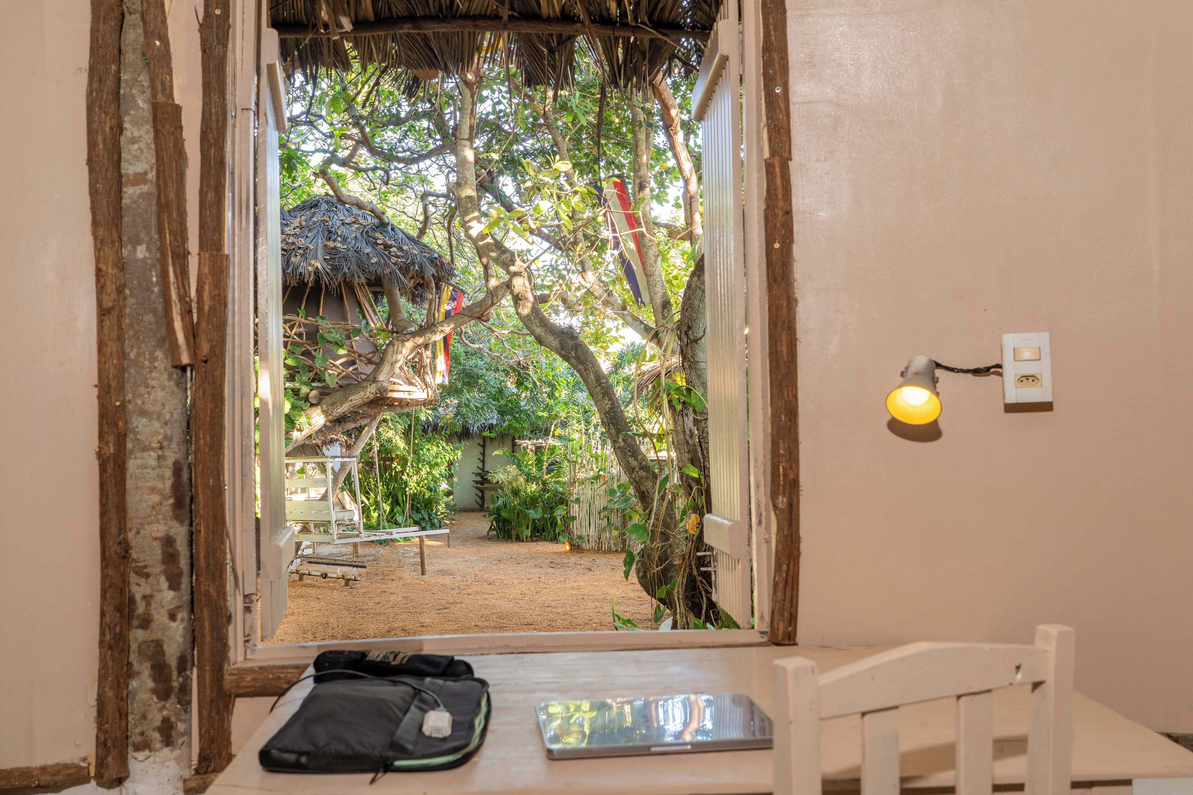 Une chambre avec une fenêtre donnant sur un jardin, un lit, une table de chevet et une prise électrique au mur.