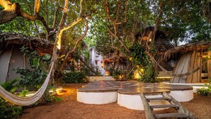 Un espace extérieur rustique agrémenté d’un hamac, d’escaliers en bois et d’une structure à toit de chaume.