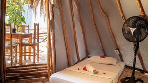 Une chambre confortable avec un lit, un ventilateur et une chaise en bois.