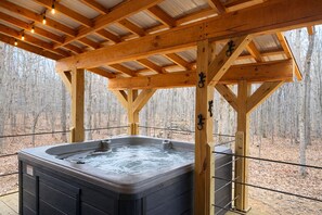 Ein Whirlpool unter einer Holzhütte mit Blick auf einen Wald.