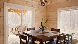 A wooden interior with a dining table, chairs, and a hanging light fixture. - Restful Haven - Hot Tub at Secluded Modern Cabin | Private Trails (Altamont)