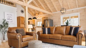 A spacious living room with leather sofas, a patterned rug, and wooden beams on the ceiling. - Restful Haven - Hot Tub at Secluded Modern Cabin | Private Trails (Altamont)