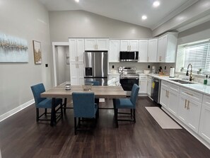 A modern kitchen with white cabinets, stainless steel appliances, and a wooden dining table with blue chairs. - Newly renovated 4-bedroom house in beautiful Covington (Covington)