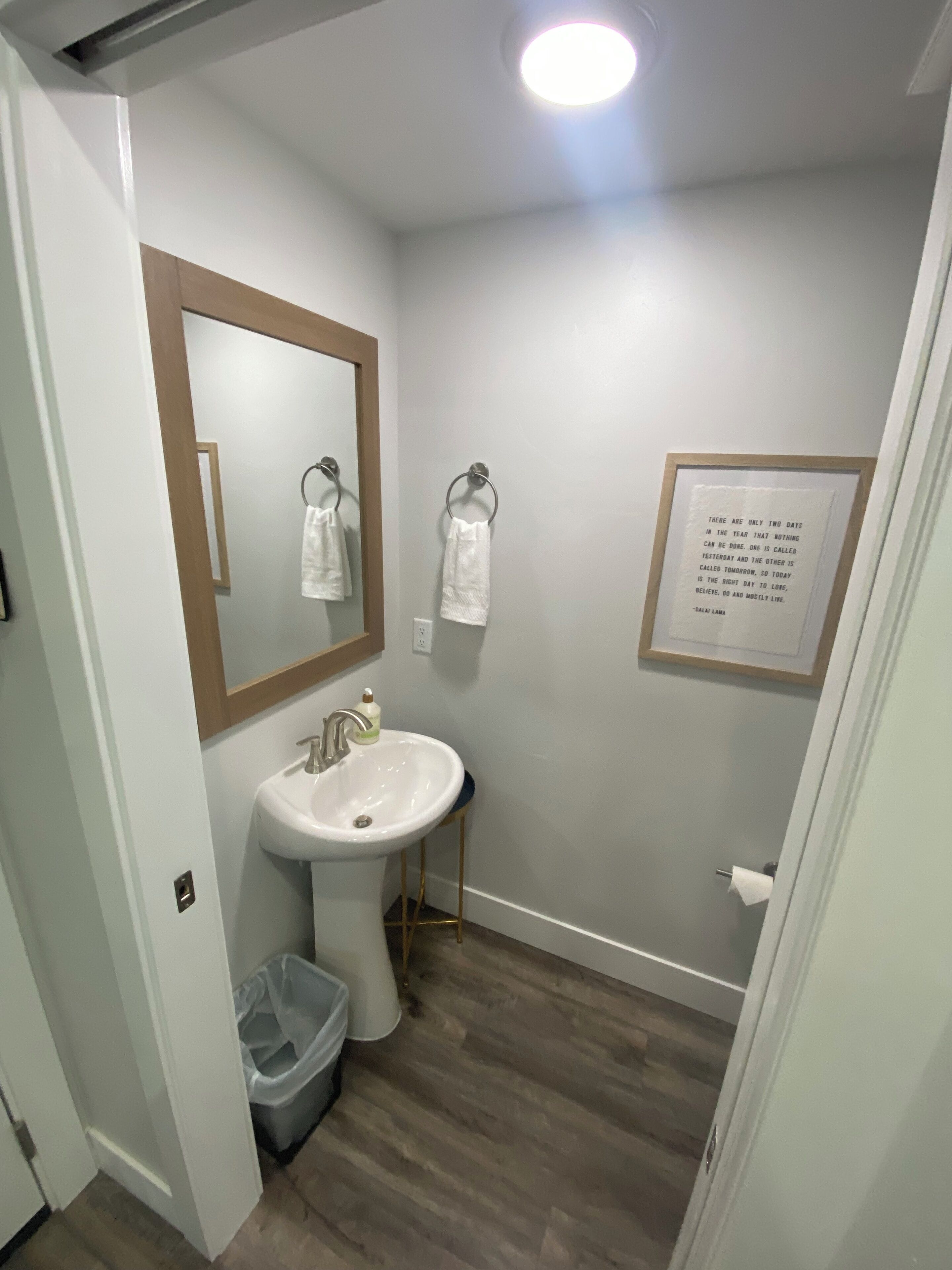A bathroom with a white sink, a mirror with a wooden frame, and a framed inspirational quote on the wall.